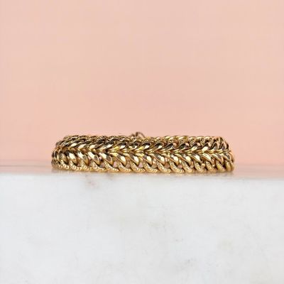 un gros plan d'un bracelet en or posé sur une surface en marbre