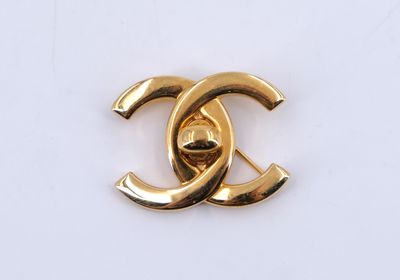 un gros plan d'une broche Chanel plaquée or sur une surface blanche