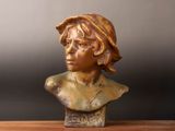 buste en bronze d'une femme coiffée d'un chapeau, posé sur une table en bois
