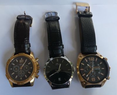 three watches are sitting on a white surface, one is black and the other is gold