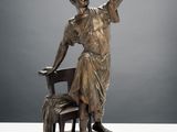 statue en bronze représentant une femme assise sur une chaise, le bras levé
