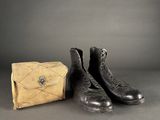 deux paires de bottes noires et un sac à main marron posés sur une surface grise