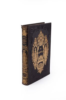 an old book with a gold and black cover sitting on a white surface