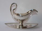 a silver gravy on a silver plate on a white surface