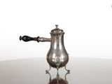 une cafetière ancienne en argent posée sur une table en verre, avec une poignée noire
