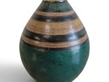 un vase vert et marron posé sur une surface blanche