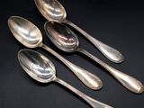 a set of four silver spoons on a black surface