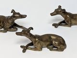 three bronze figurines of greyhounds laying down on a white surface