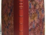 an old book with a red cover sitting on top of a white table