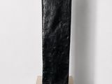 sculpture of a black stone block on a wooden stand on a white wall