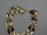 a gold and black bracelet with square links on a grey background