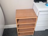 a small wooden shelf next to a bed in a room