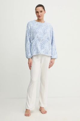a woman standing in front of a white background wearing a blue sweater and white pants