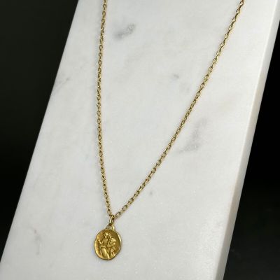 un collier en or orné d'une pièce de monnaie, posé sur une surface en marbre blanc