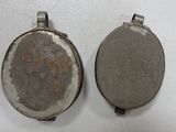 two silver metal oval pendants on a white surface