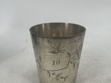 a silver cup with a design on it sitting on a white surface