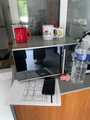 un micro-ondes posé sur un plan de travail, à côté d'un verre d'eau et d'un téléphone portable