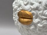 a close up of a white and gold sheep statue on a white surface