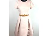 Le mannequin porte une robe avec une ceinture dorée.