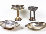 trois bols en métal argenté et un bougeoir posés sur une surface blanche