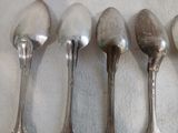 quatre cuillères en argent sont alignées sur une surface blanche