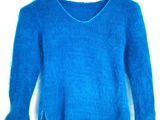 Le pull est bleu et présente des bords effilochés au niveau des manches.