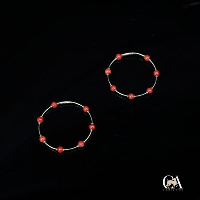une paire de boucles d'oreilles créoles ornées de perles rouges sur fond noir