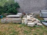 un tas de bois posé dans l'herbe, près d'un mur de briques