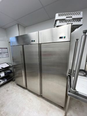 des réfrigérateurs en acier inoxydable dans une cuisine professionnelle, à côté d'une étagère métallique