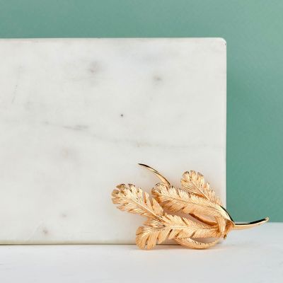 broche en feuille d'or posée sur un bloc de marbre blanc