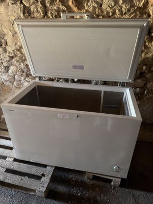 un congélateur coffre blanc posé sur une palette devant un mur en pierre