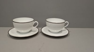 deux tasses et soucoupes posées sur une table, sur fond gris