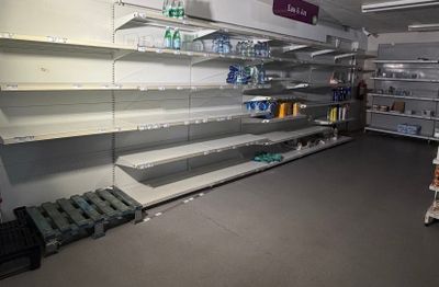 de nombreuses étagères vides dans un magasin, sur lesquelles sont posées des bouteilles d'eau