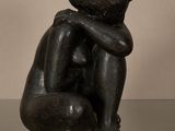 statue d'une femme assise sur une table en verre, les mains posées sur les genoux