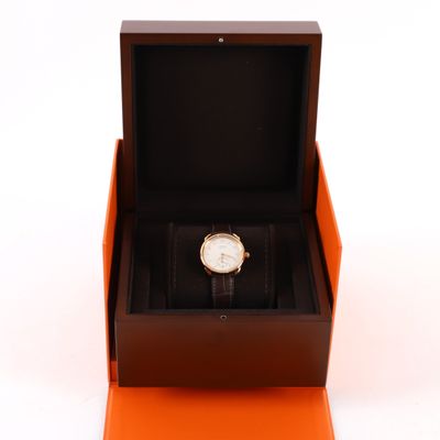 une boîte orange contenant une montre, posée sur une surface blanche