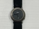 une montre noire avec un bracelet noir posée sur une surface blanche