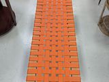 un banc tissé de couleur orange posé sur un sol blanc