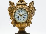 une horloge dorée posée sur un socle, sur fond blanc