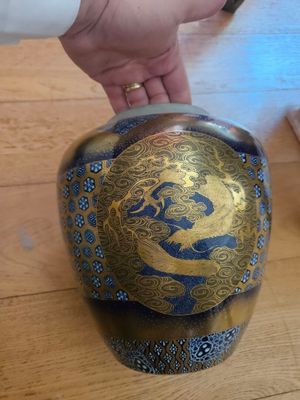 une personne tenant un vase bleu et doré posé sur une table en bois