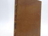 an old book with a brown cover sitting on a white surface