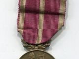 médaille violette et dorée sur fond blanc, accompagnée d'un ruban rouge