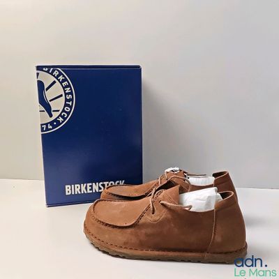 Les chaussures marron se trouvent à côté d'une boîte bleue, posée sur une surface blanche.