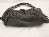 grey sued purse with fringes on top of it on a bed