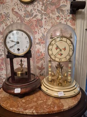 deux horloges posées sur une table recouverte d'une cloche en verre