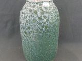 un vase vert posé sur une table sur fond noir