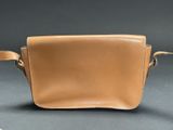 tan leather cross body bag with adjustable shoulder strap on grey background