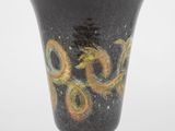 vase noir orné de motifs jaunes et verts sur un fond blanc