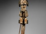 une vieille figurine en bois représentant un homme assis au bout d'un bâton en bois