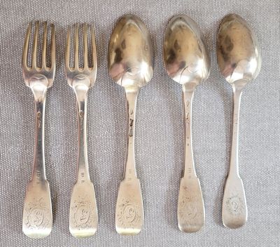 cinq cuillères en argent et une fourchette sont alignées sur une table