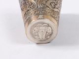 a silver vase with a coin on it on a white surface